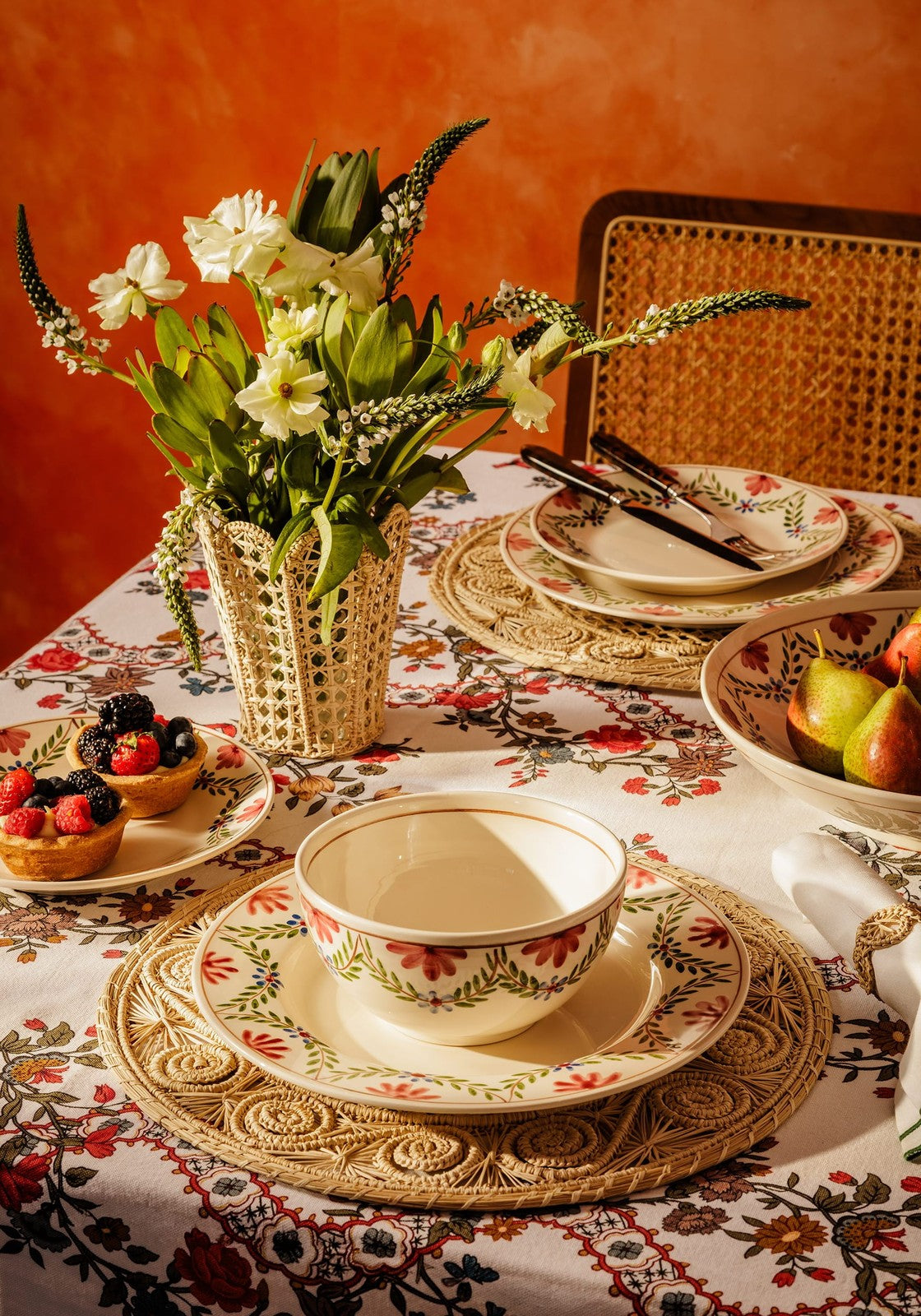 Cream-colored ceramic camilla cereal bowl with red and green floral pattern on an ornate woven placemat