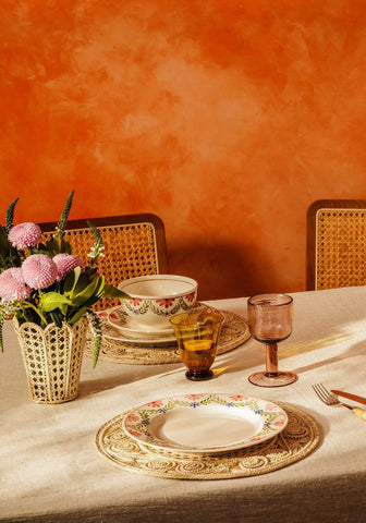 A green garland camilla cereal bowl beside a delicate woven wicker vase holding soft pink flowers