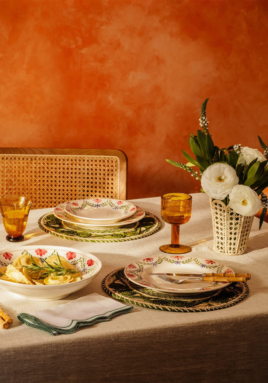 A white ceramic camilla salad bowl with green garland trim filled with pasta garnished with rosemary