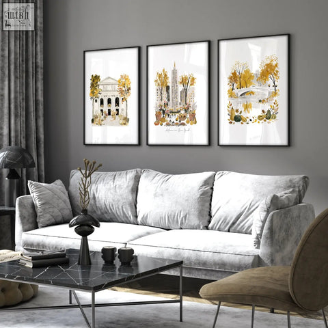 Three framed autumn-themed watercolor art prints with black frames hanging above a gray velvet sofa in living room wall art