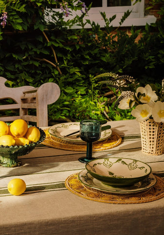 A ceramic cara shell bowl with a green rim and floral cream pattern on an ornate woven placemat