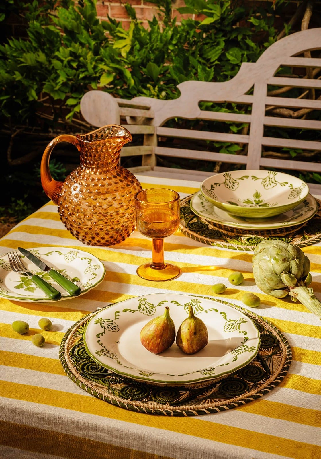 Amber-colored textured glass pitcher with curved handle and spout next to green cara shell pasta bowl