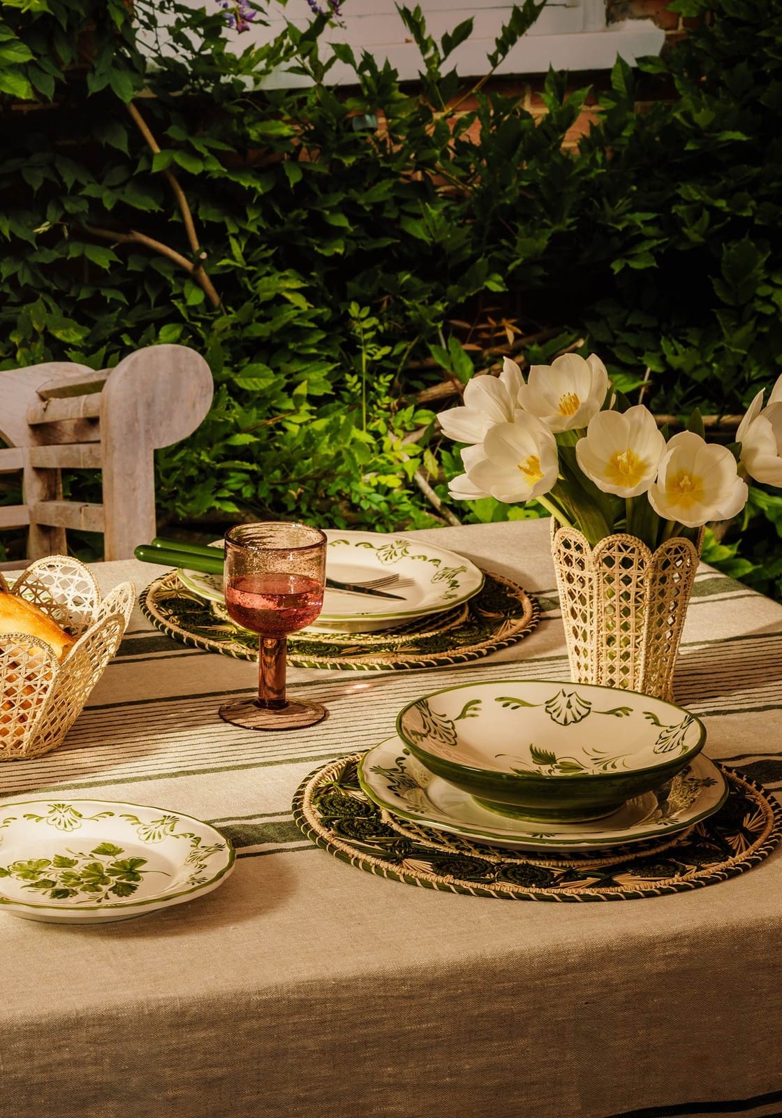A cream ceramic pasta bowl with a green rim and leafy patterns resting on an ornate woven placemat