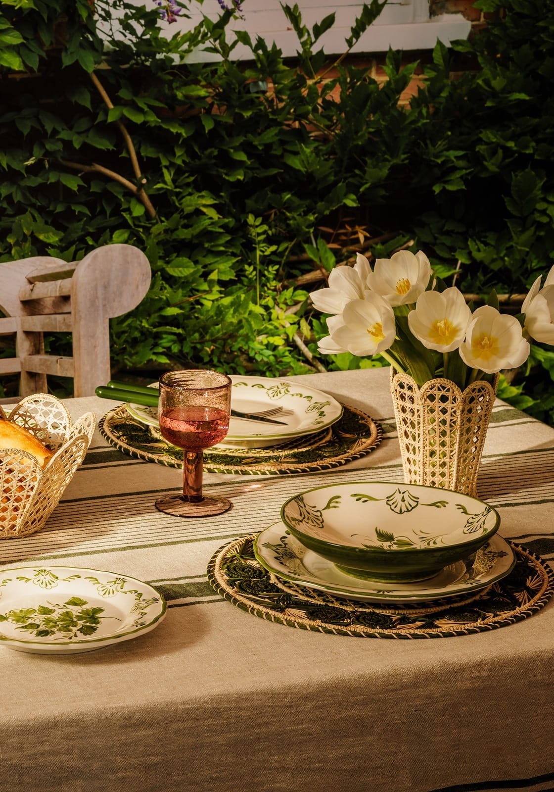 A cream-colored ceramic pasta bowl with a green rim and hand-painted botanicals on a woven placemat