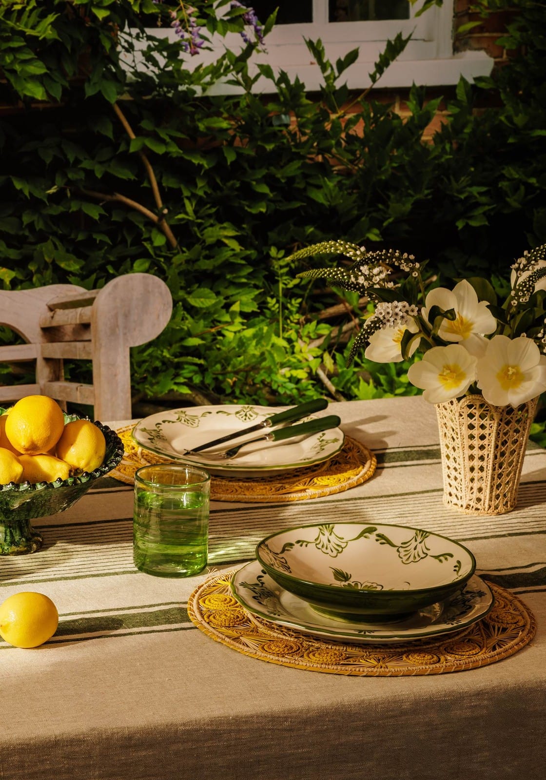 White ceramic cara shell pasta bowl with green floral leaf patterns on woven placemats
