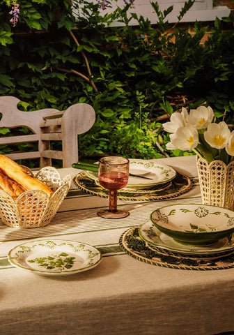A cara shell dinner set featuring green and white ceramic shell dinner plates and matching bowl on striped cloth