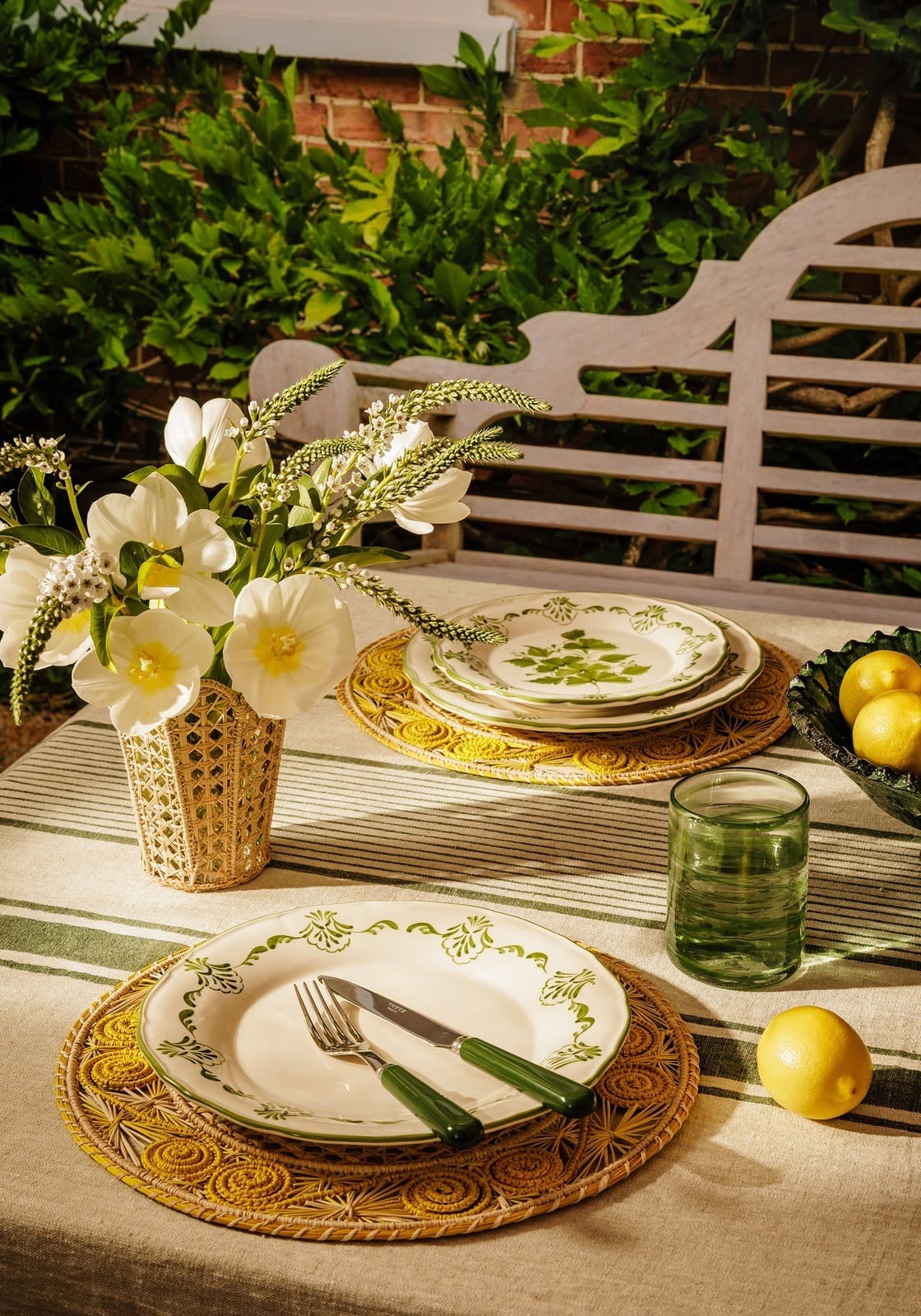 A white ceramic cara shell side plate with green leafy patterns resting on a woven yellow placemat