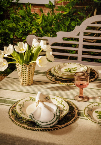 White tulips in a woven beige vase next to a green cara shell dinner plate with shell dinner plate design