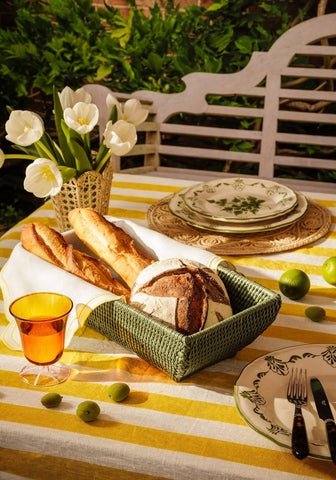 Green woven basket holding baguettes and bread next to a green cara shell dinner plate for shell dinner setup