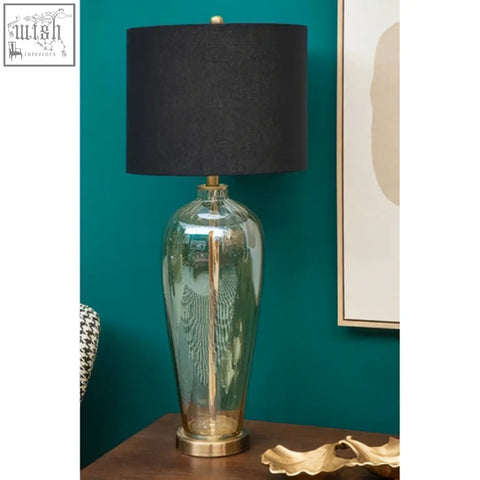 Carina amber glass table lamp with tall translucent green glass body, black fabric shade, and brass accents