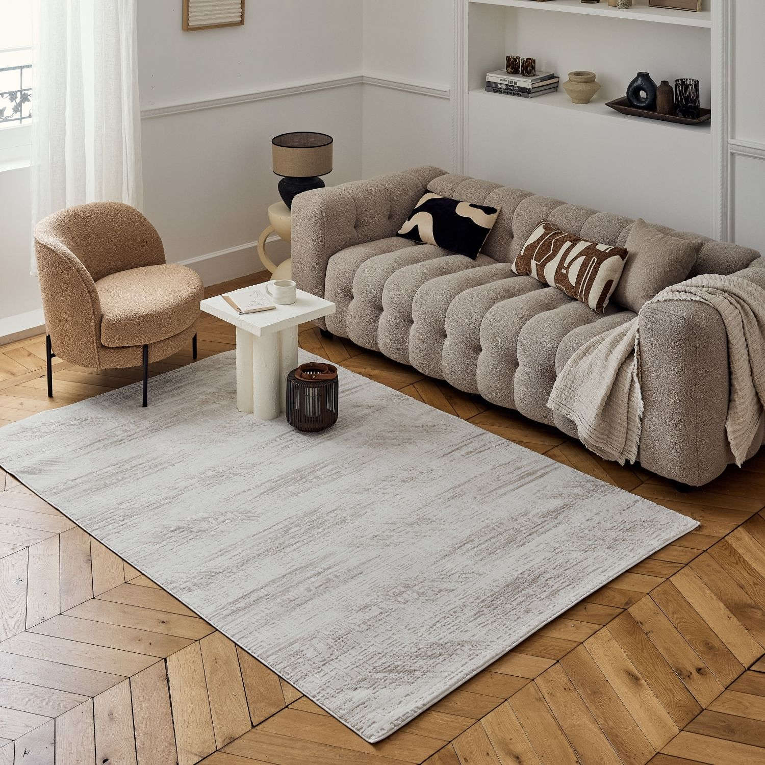 Beige tufted sofa with plush textured surface and rounded armrests next to carmel cream-beige abstract rug