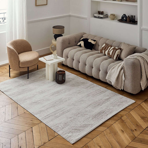 Beige tufted sofa with plush textured surface and rounded armrests next to carmel cream-beige abstract rug