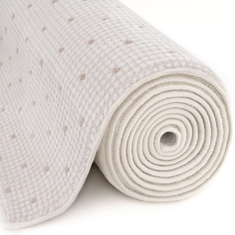 A rolled-up white memory foam mattress topper with a perforated surface shown with carmel cream-beige dots rug
