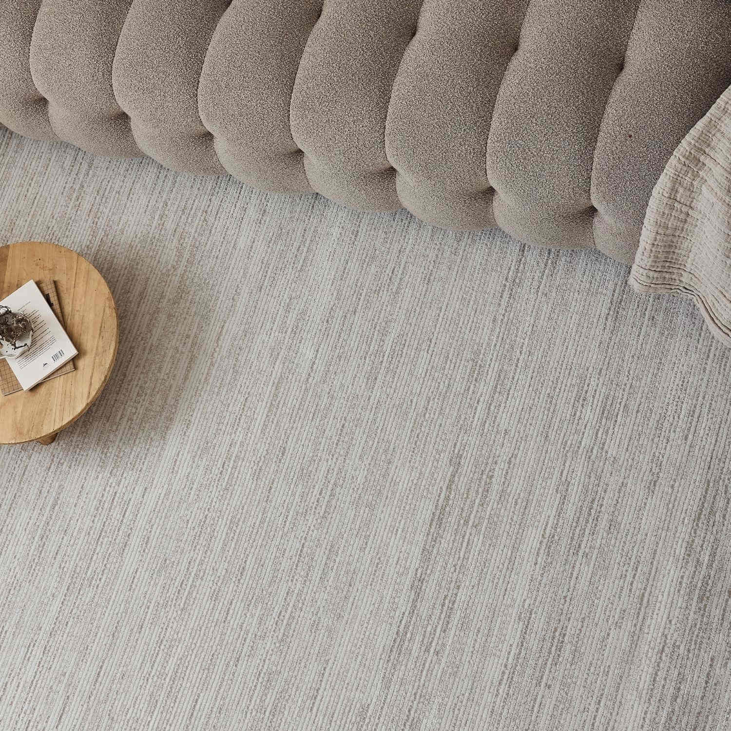Beige tufted cushion with a soft textured surface and rounded edges shown on a carmel cream-beige striped rug
