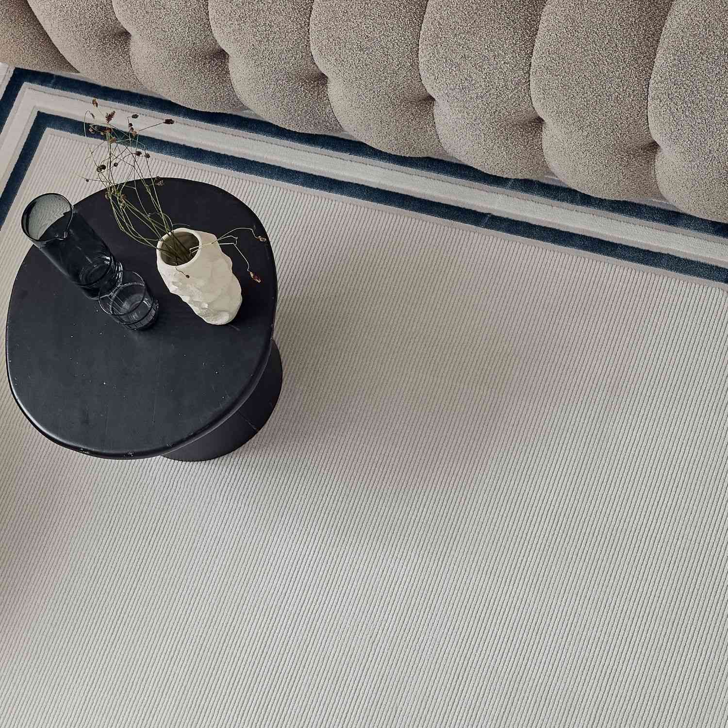 Black round side table with matte finish and minimalist design next to a carmel cream blue bordered rug