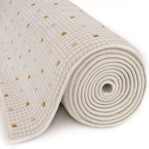 A rolled-up off-white bath mat with a textured woven surface and gold dots rug perfect for bathroom decor