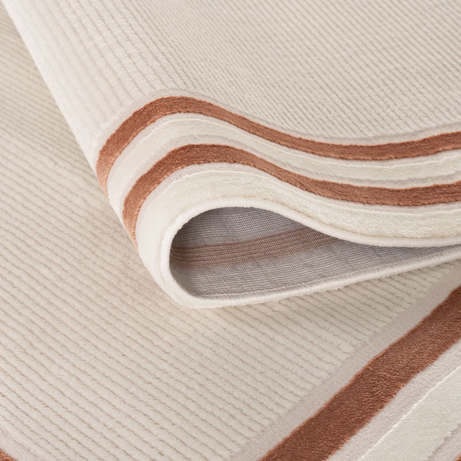 Cream-colored bordered rug with textured ribbed surface and two rust-brown stripes along the edge from carmel cream-terra