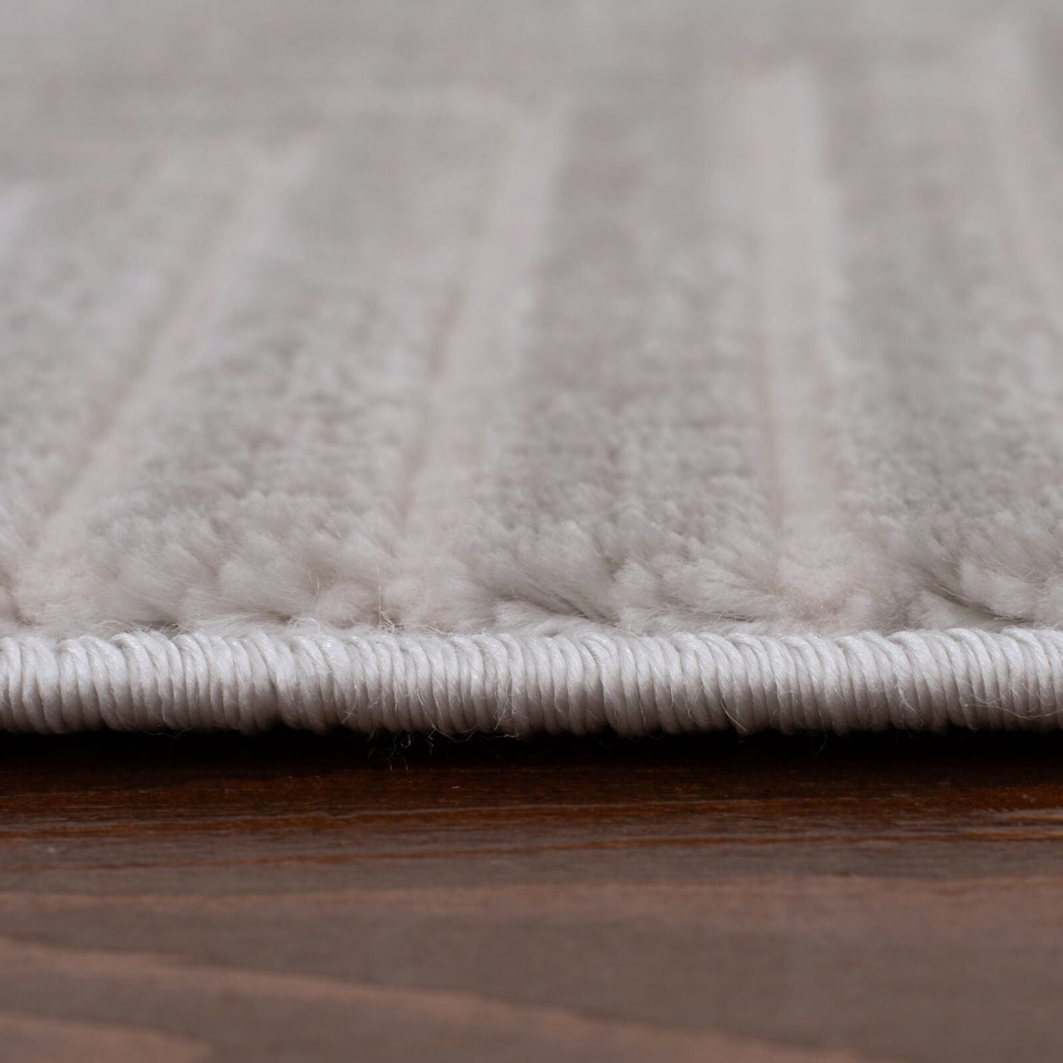 White plush geometric rug with soft textured fibers and neatly stitched border in carmel grey-cream tones