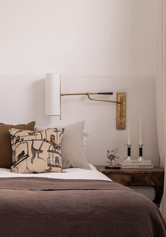 Brass wall-mounted reading lamp with adjustable arm and white cylindrical shade shown with Carsons classic candle holders