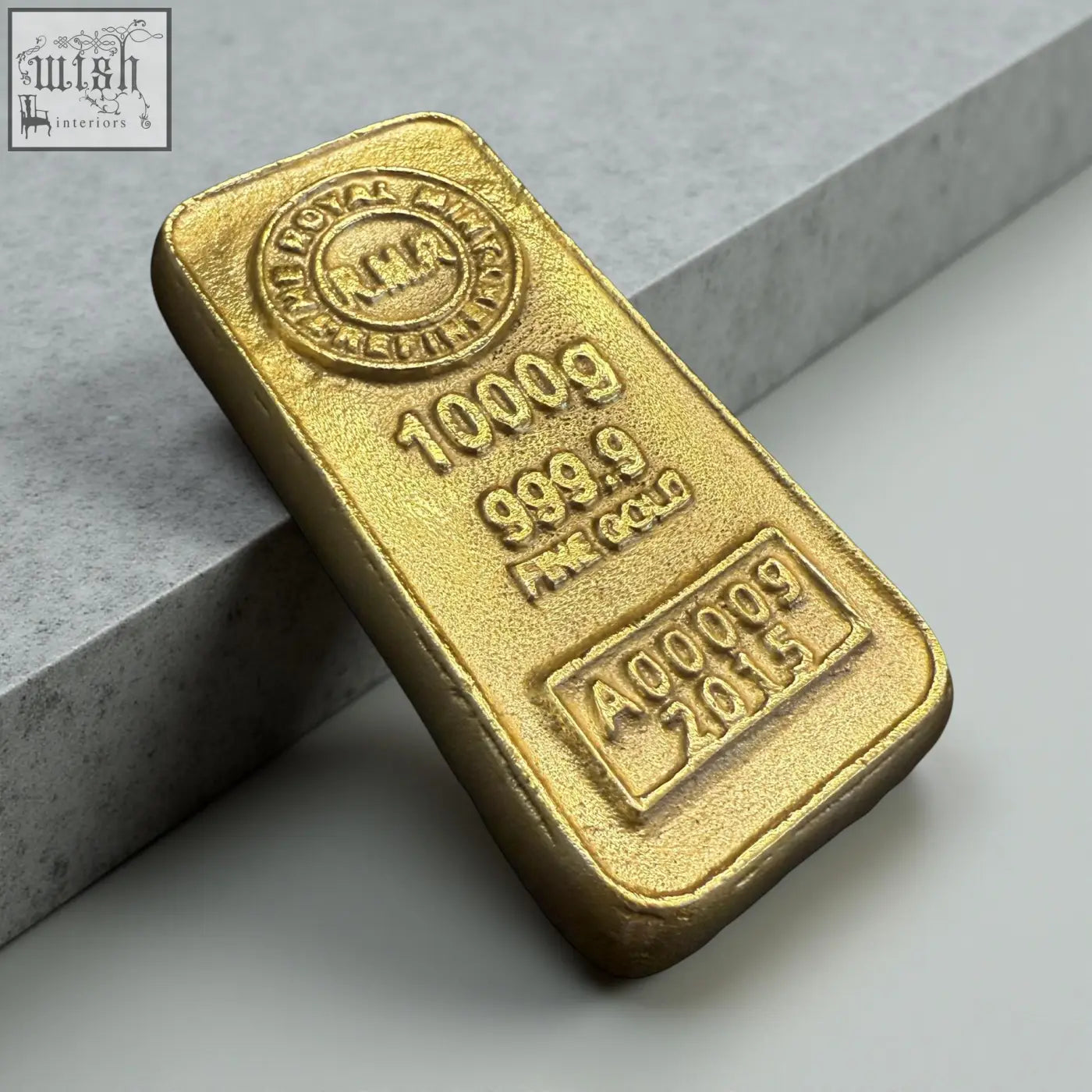 A polished 1000g royal mint gold bar with serial a000092815 used as a solid cast aluminium gold bullion paperweight