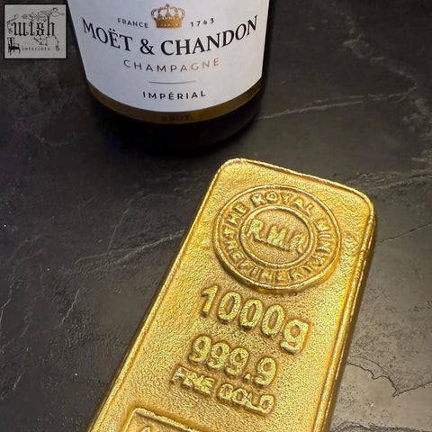 A solid cast aluminium gold bullion bar paper weight shaped like a gleaming 1000g fine gold bar with moët champagne