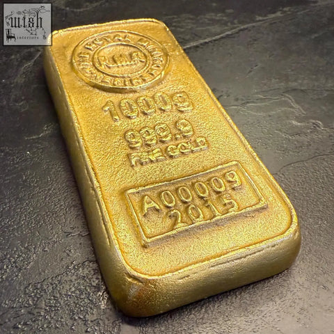 A 1000g polished royal mint gold bar with engraved purity and serial number used as a cast aluminium paperweight