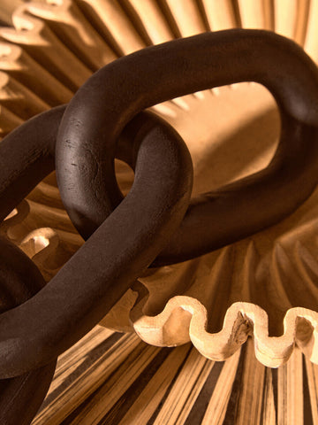 Dark matte black wood link chain decor with interlocking links resting on a light wooden fan structure