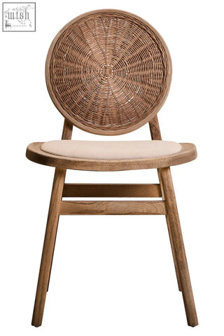 A rustic dining chair with a circular woven rattan back and beige fabric seat in white wash elm wood