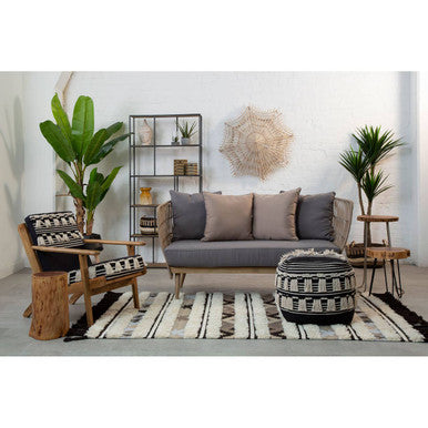Gray upholstered sofa with beige cushions and a woven striped cefena black pouffe ottoman in front