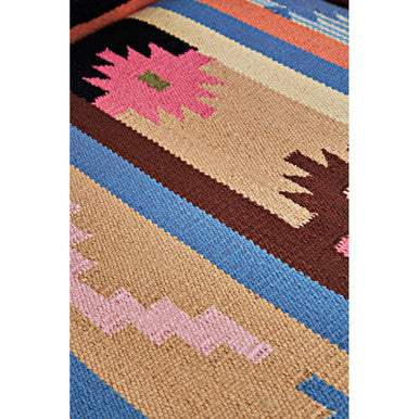 A vibrant kilim rug with bold geometric patterns placed under a cefena multi coloured fabric chair with mango wood legs