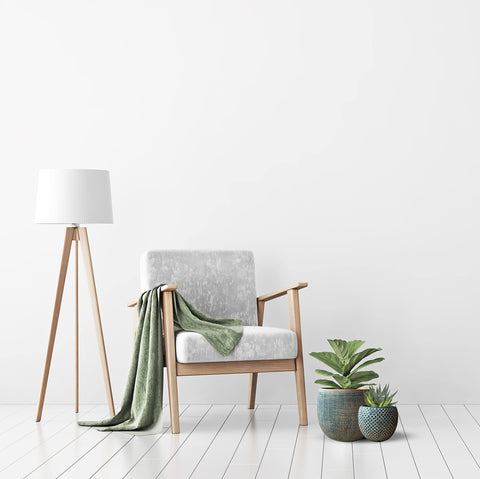 Modern wooden armchair with gray fabric seat and olive green throw beside ceramic green gold plant pot set for indoor use