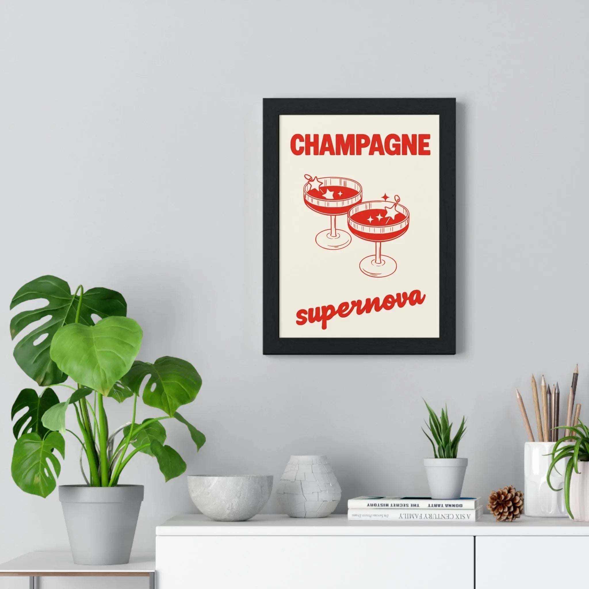 Black-framed champagne supernova poster with red text and champagne glasses on cream oasis inspired wall art