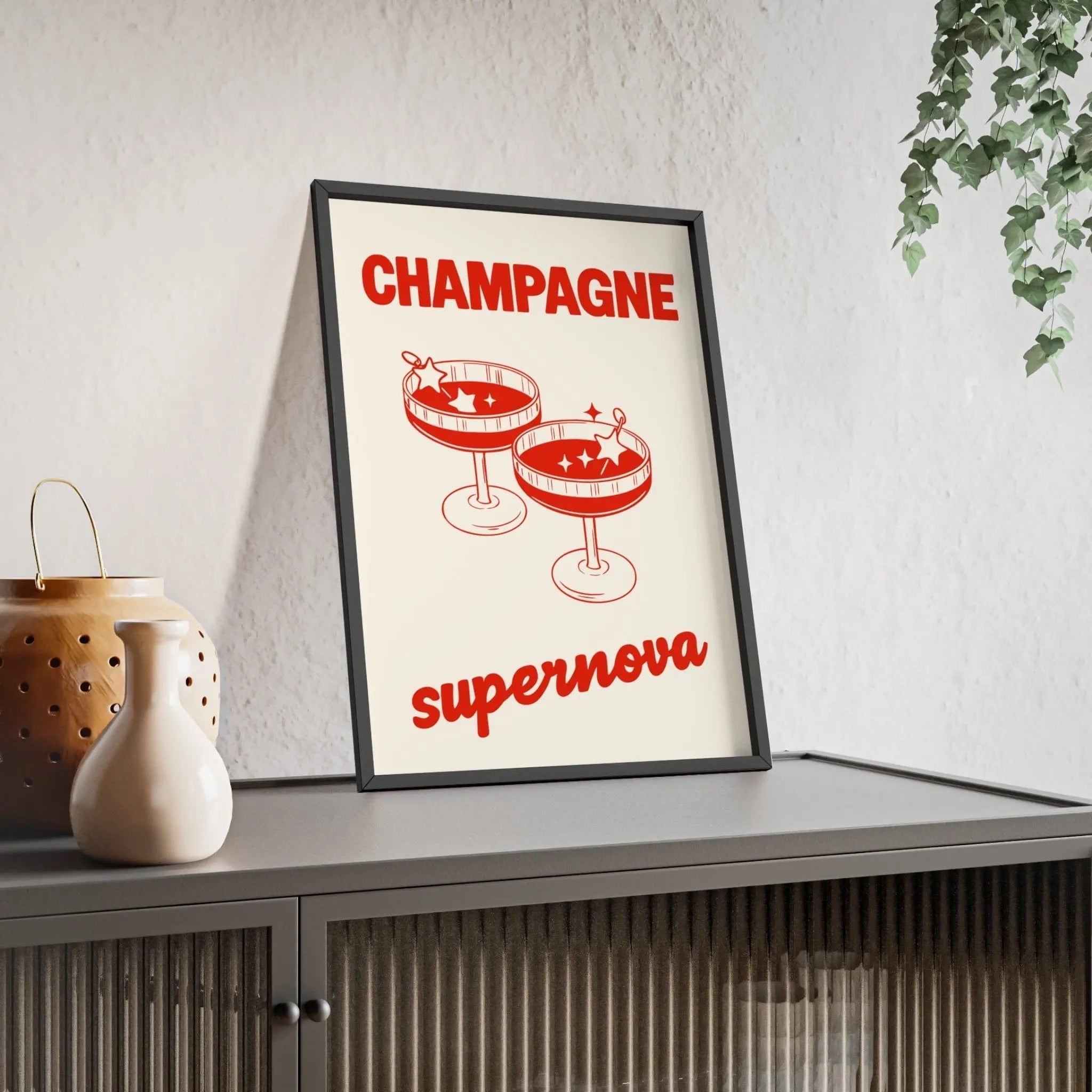 A framed champagne supernova poster with bold red text and two champagne flutes on a cream oasis inspired background