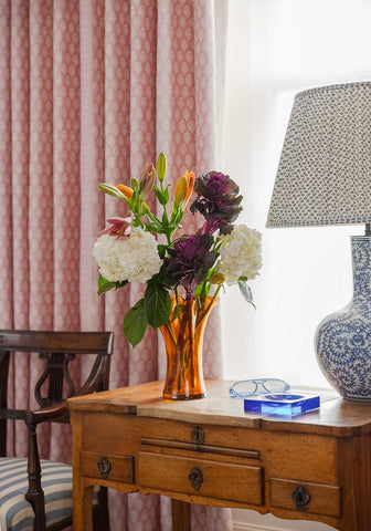 An amber glass vase with white hydrangeas and orange lilies beside a chelsea cobalt glass trinket tray blue