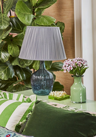 A blue textured glass table lamp with a pleated gray white shade near a yellow green glass trinket tray