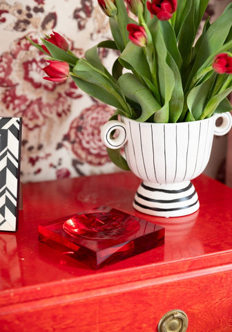 White ceramic vase with black stripes and circular handles next to chelsea sweet glass red trinket tray