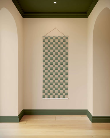 A rectangular chequerboard wall hanging tapestry with green and beige squares framed by a white border