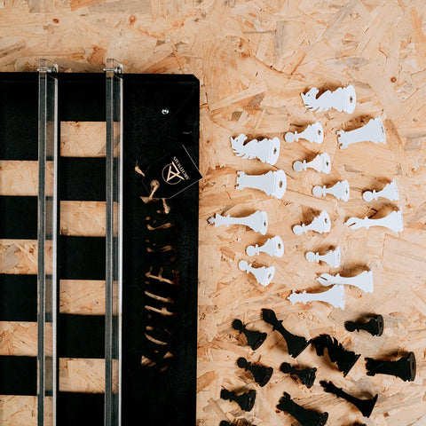 White and black sleek modern chess wall game pieces arranged on wooden surface with two squares visible