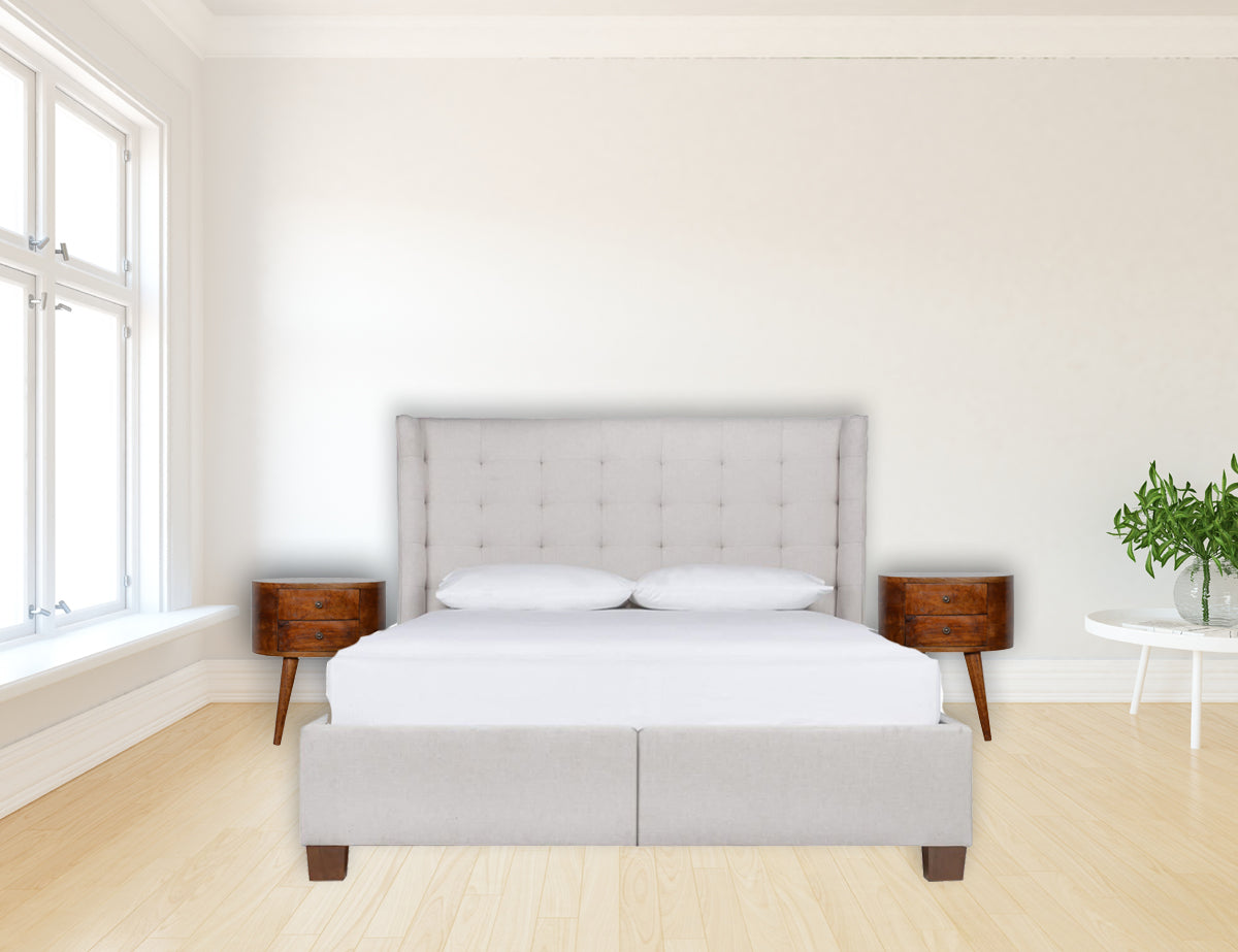 A sleek light gray upholstered bed with tufted headboard and footboard next to a chestnut rounded bedside table