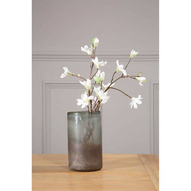 Chiara medium grey sand effect vase in translucent gray glass holds white magnolia blossoms on slender branches with natural hevea wood accents