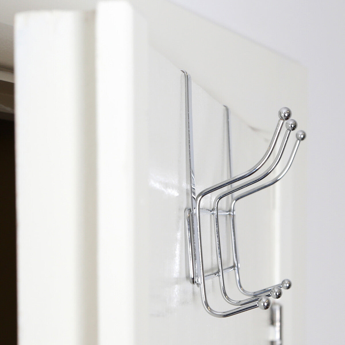 Chrome finished metal door six hook hanger with four curved hooks and spherical tips mounted on a white surface