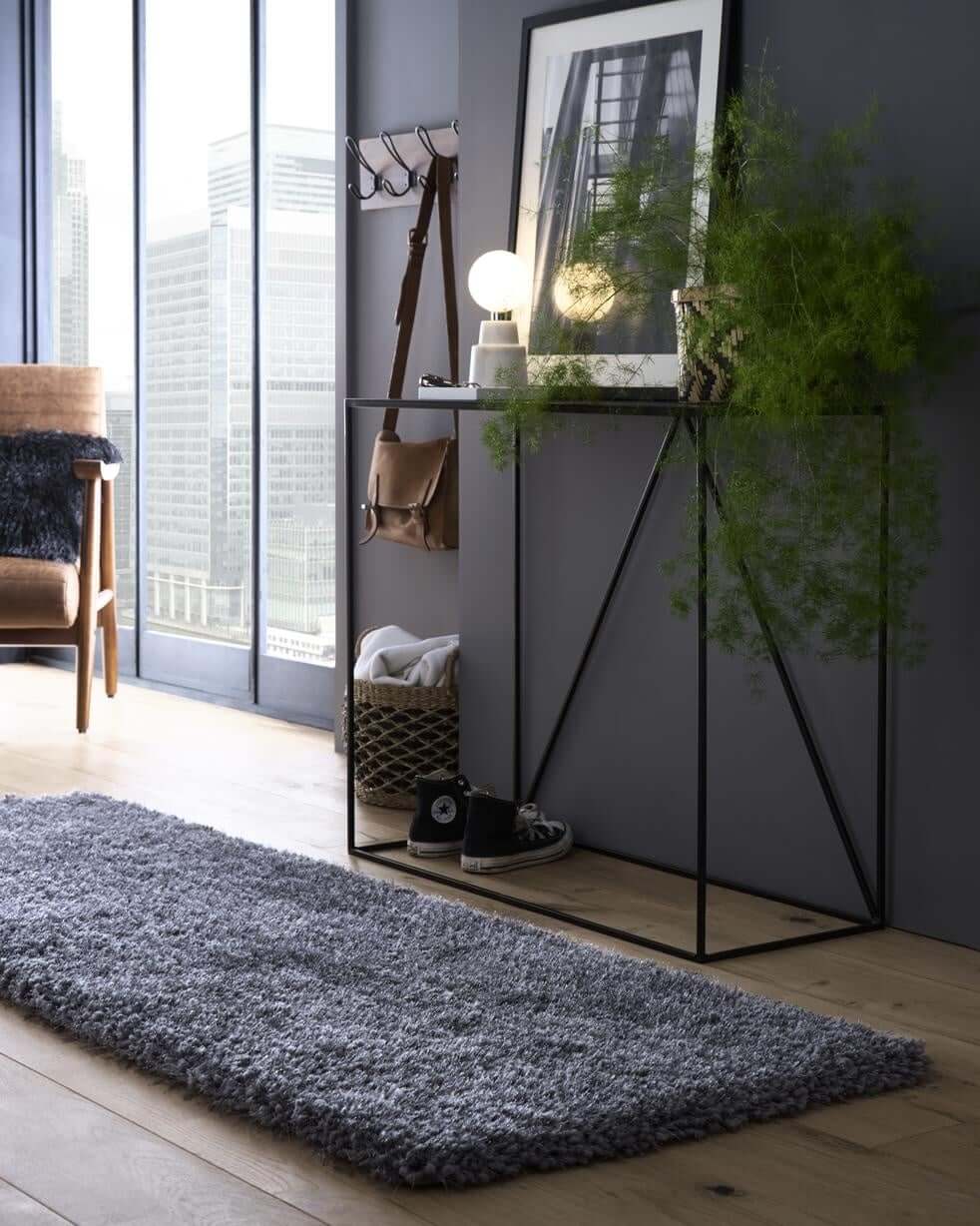 A sleek black metal console table with a hanging brown leather bag standing on a chicago grey shaggy rug