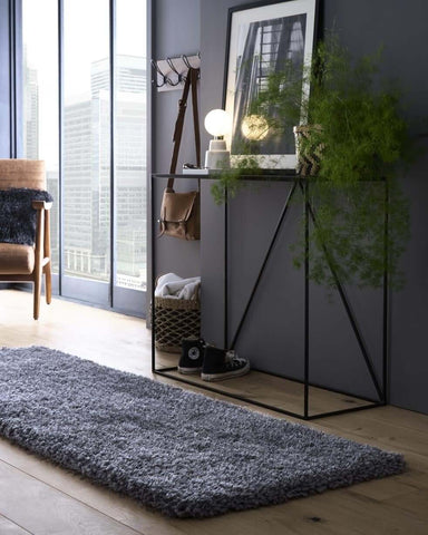 A sleek black metal console table with a hanging brown leather bag standing on a chicago grey shaggy rug