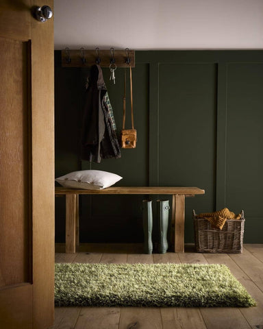 A rustic wooden bench with natural finish sitting on a chicago olive green shaggy rug with soft olive green tones