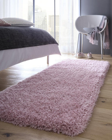 A plush chicago pink shaggy rug with a soft fluffy texture lies on a wooden floor showing its light pink color