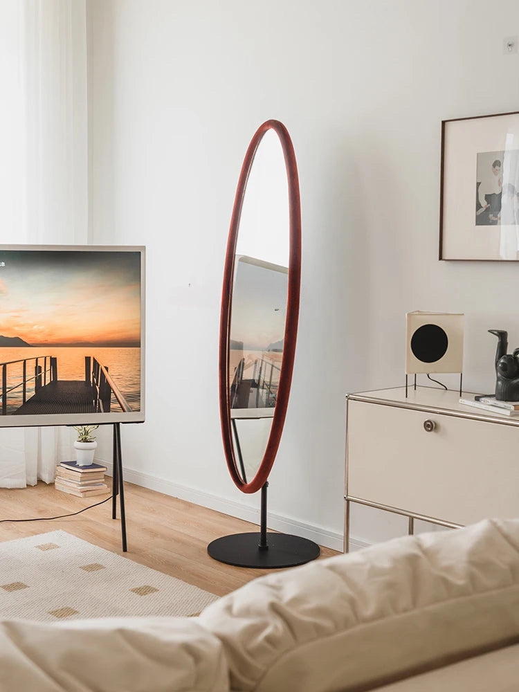 A tall oval chinatsu mirror with a sleek red frame and black stand perfect for modern home decor