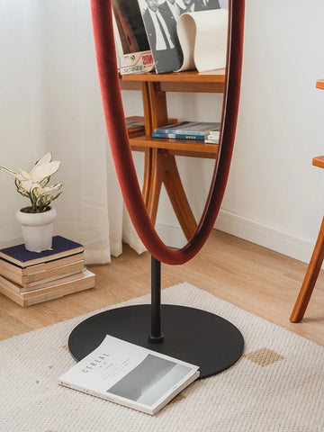 A tall oval chinatsu mirror with a red velvet frame and black metal stand perfect for stylish home decor