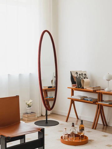 A tall chinatsu mirror with an oval reddish brown wooden frame and a sleek black circular base perfect for any room