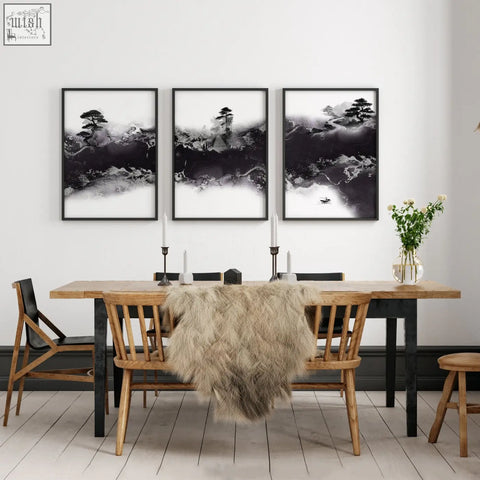 Three black and white chinese artwork prints of bonsai and misty mountains hang above a wooden dining room table