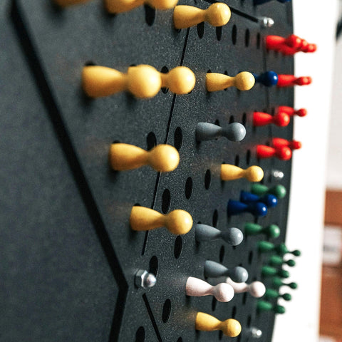 A black chinese checkers wall game with colorful wooden pawns set in an opposite triangle pattern on a pegboard